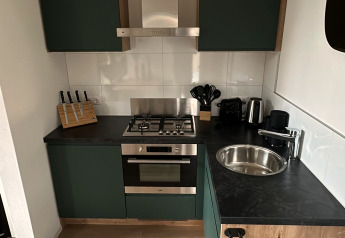 Moderne compacte keuken in Tiny Lodge bij Veluwepark de Bosgraaf, met groene kasten en houtaccenten.