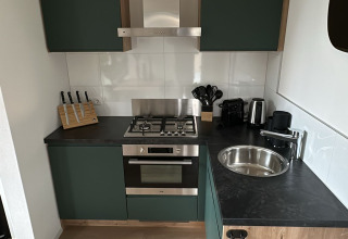 Modern small kitchen in Tiny Lodge at Veluwepark de Bosgraaf, featuring green cabinets and wood accents.