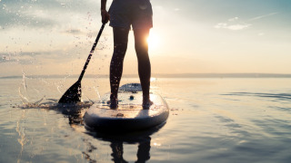 Personne en paddle sur un lac au coucher du soleil, prise dans un parc de vacances avec hébergement glamping.