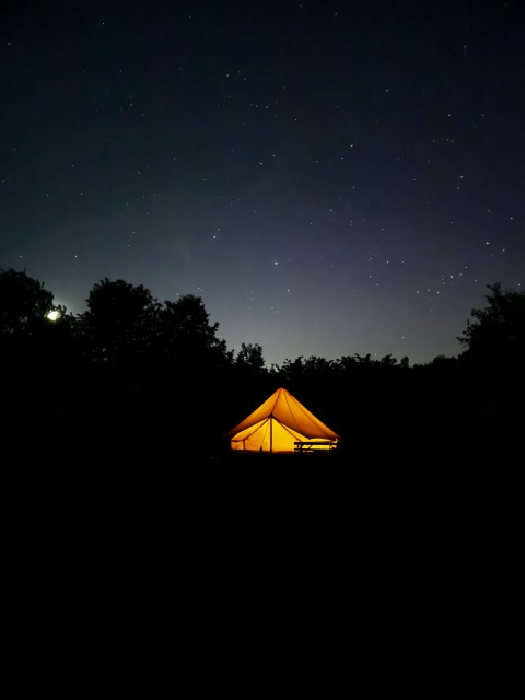 Verlichte safaritent Bell Tent 500 bij REBL Outdoor in Nederland met een sterrenhemel erboven.