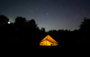 En oplyst safariteltscene i mørket under stjernerne, Bell Tent 500 ved REBL Outdoor i Holland.