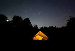 En oplyst safariteltscene i mørket under stjernerne, Bell Tent 500 ved REBL Outdoor i Holland.
