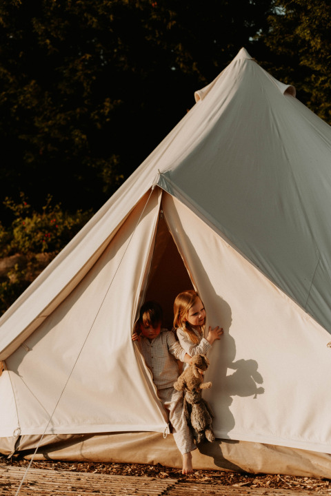 Dos niños en pijama salen de la Bell Tent 500 de REBL Outdoor en los Países Bajos al amanecer.