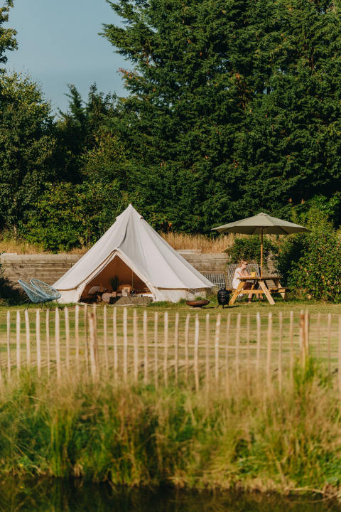Tienda de safari Bell Tent 500 en REBL Outdoor, Países Bajos, con mesa de picnic y entorno verde exuberante.