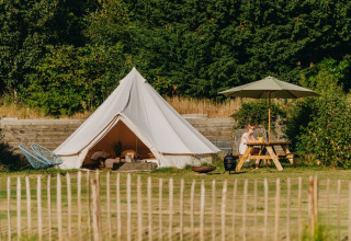 Tienda de safari Bell Tent 500 en REBL Outdoor, Países Bajos, con mesa de picnic y entorno verde exuberante.