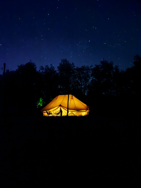 Tienda safari Bell Tent Emperor iluminada de noche bajo un cielo estrellado en REBL Outdoor, Países Bajos.