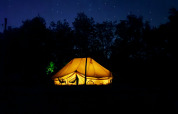 Tienda safari Bell Tent Emperor iluminada de noche bajo un cielo estrellado en REBL Outdoor, Países Bajos.