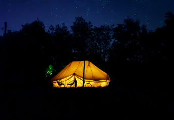 Tienda safari Bell Tent Emperor iluminada de noche bajo un cielo estrellado en REBL Outdoor, Países Bajos.