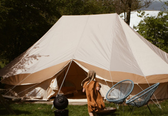 Un niño corre hacia la tienda safari Bell Tent Emperor en REBL Outdoor, Países Bajos, rodeado de árboles.