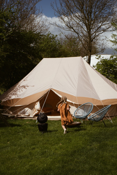 Et barn løber mod et stort safaritelte, Bell Tent Emperor, hos REBL Outdoor i Holland, omgivet af træer.