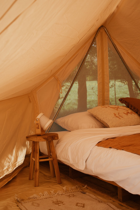 Interior de la tienda Bell Tent Emperor en REBL Outdoor, Países Bajos, con cama acogedora y decoración rústica.