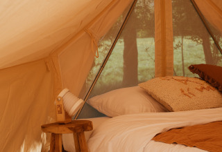 Interior de la tienda Bell Tent Emperor en REBL Outdoor, Países Bajos, con cama acogedora y decoración rústica.