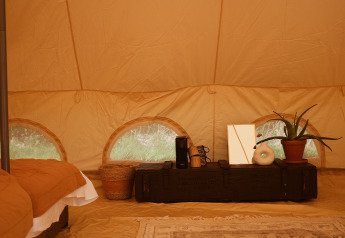 Indretning af Bell Tent Emperor safari telt hos REBL Outdoor, med seng, planter og dekorative elementer.