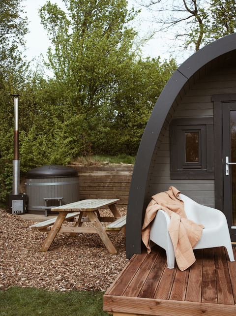Glamping pod with hot tub, picnic table, and blanket on chair at REBL Outdoor, Netherlands, in nature.