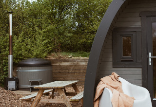 Udendørs glamping pod med boblebad, træmøbler og tæppe i REBL Outdoor, Holland, omgivet af natur.