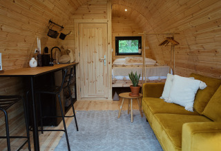 Gezellige glamping pod met houten afwerking, bank, tafel, bed en rek bij REBL Outdoor in Nederland.