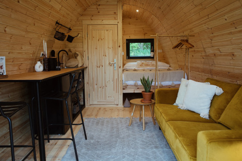 Cozy interior of a glamping pod with wood finish, yellow sofa, bed, and bar at REBL Outdoor, Netherlands.