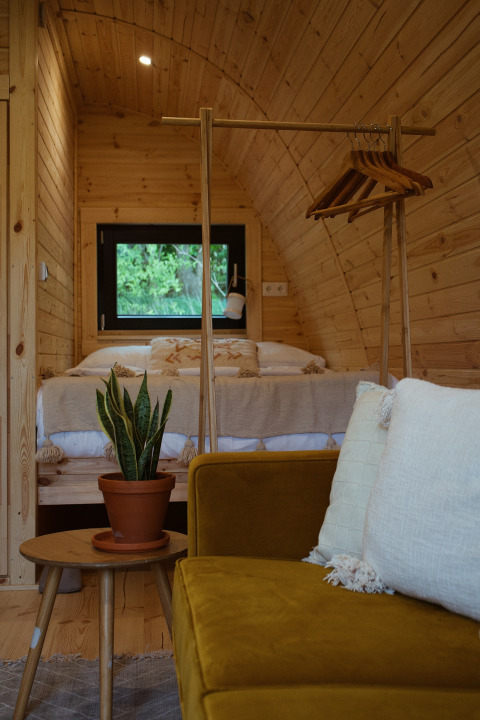Inde i en hyggelig glamping pod med træpaneler, en komfortabel seng, planter og varme farver.