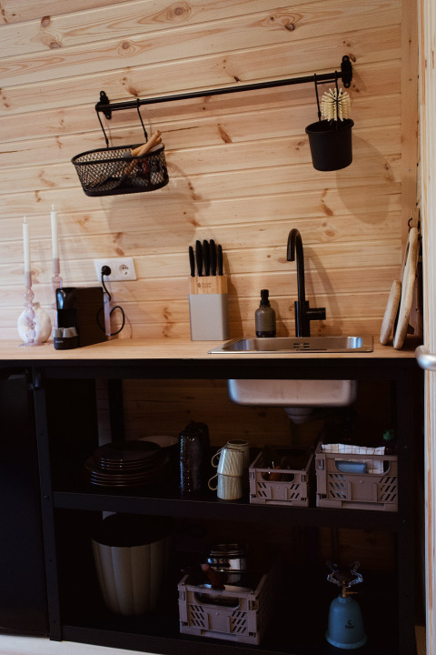 Kleine keuken met houten wand, zwarte spoelbak en open rekjes in een glamping pod in Nederland.