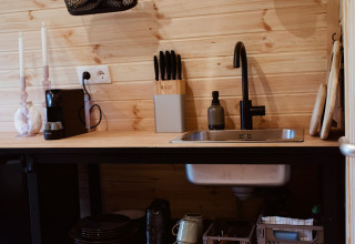 Kleine keuken met houten wand, zwarte spoelbak en open rekjes in een glamping pod in Nederland.