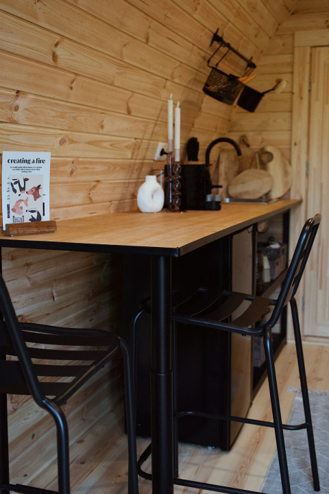 Gezellige houten binnenruimte met moderne barkrukken en tafel in een glampingpod met hot tub in Nederland.