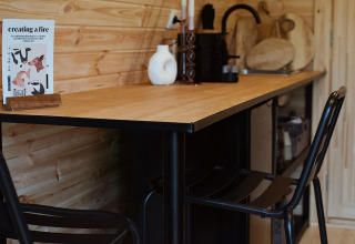 Gezellige houten binnenruimte met moderne barkrukken en tafel in een glampingpod met hot tub in Nederland.