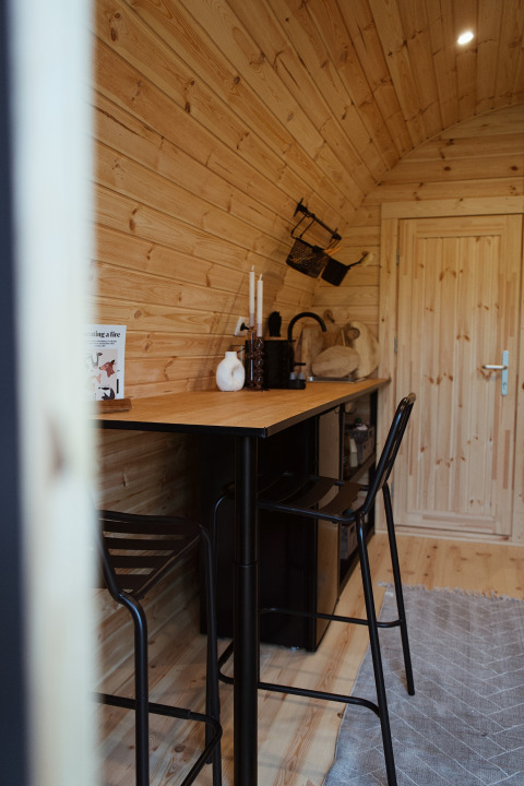 Inde i en hyggelig træbeklædt glamping pod med højt bord, stole og indrettet køkkenområde i Holland.