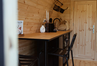 Binnenkant van een knusse houten glamping pod met hoge tafel en stoelen bij REBL Outdoor in Nederland.