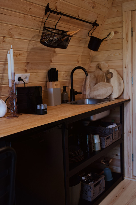 Moderne tekøkken i en glamping pod med trævægge, sorte hylder og køkkenredskaber i REBL Outdoor.