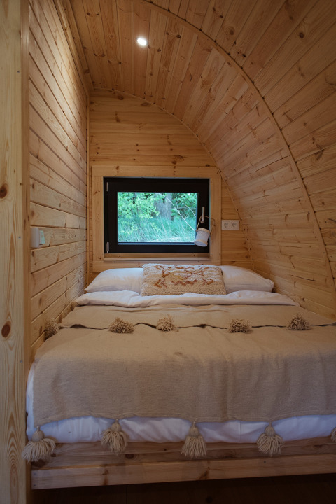 Cozy wood-paneled glamping pod with a double bed and window at REBL Outdoor in the Netherlands.