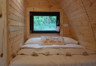 Cozy wood-paneled glamping pod with a double bed and window at REBL Outdoor in the Netherlands.