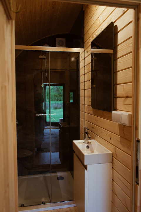 Badkamer in een glampingpod met houten wanden, douche en zicht op de groene buitenomgeving.