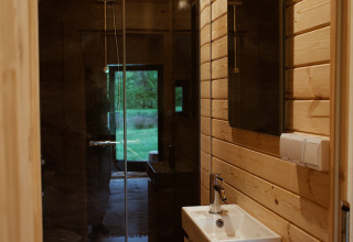 Badkamer in een glampingpod met houten wanden, douche en zicht op de groene buitenomgeving.