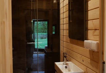 Badeværelse i en glamping-pod med trævægge, brusekabine og udsigt til det grønne udendørs.
