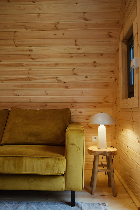 Modern glamping pod interior at REBL Outdoor Netherlands, featuring a yellow sofa, lamp, and wood table.