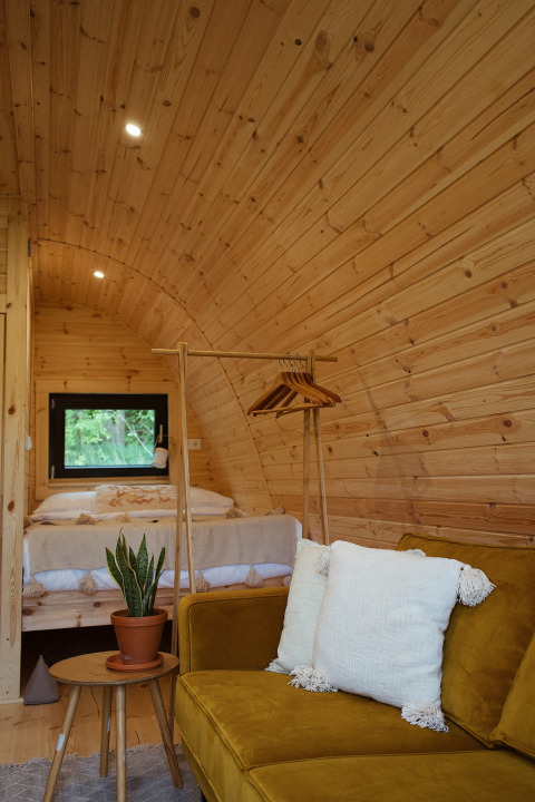 Indretning af Glamping Pod med trævægge, grøn sofa, hvid pude og indendørs plante ved REBL Outdoor.