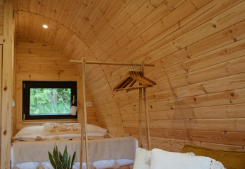 Interior de una Glamping Pod con paredes de madera, sofá amarillo, cojines blancos y planta, en REBL Outdoor.