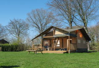 Tienda safari Ranger Lodge en el Recreation Park Den Blanken en Países Bajos rodeada de césped y árboles.
