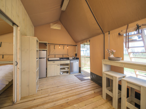 Vista interior de una tienda safari Ranger Lodge con suelo de madera, cocina y comedor en los Países Bajos.