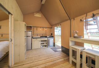 Vista interior de una tienda safari Ranger Lodge con suelo de madera, cocina y comedor en los Países Bajos.