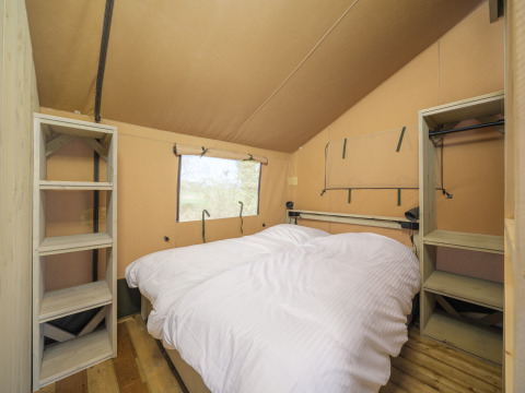 Slaapkamer in een Ranger Lodge safaritent met dubbel bed en rekken bij Recreation Park Den Blanken.