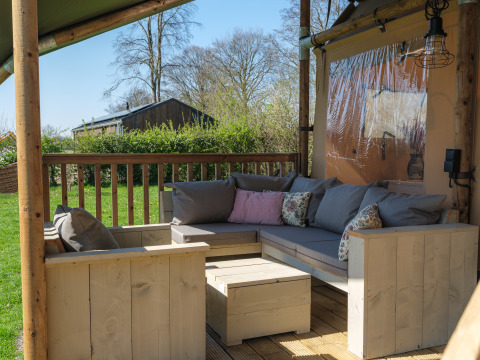 Zona de estar exterior con muebles de madera y cojines en la terraza de Ranger Lodge en Den Blanken, Países Bajos.
