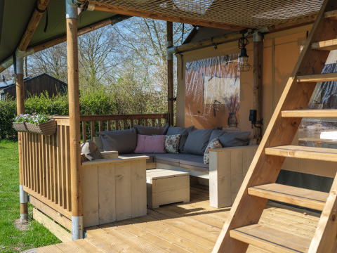 Houten terras met loungehoek en trap bij de Ranger Lodge safaritent op Park Den Blanken in Nederland.