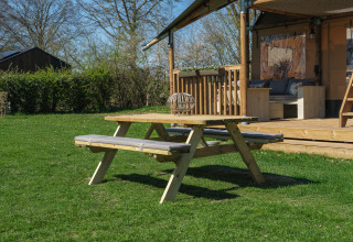 Picknickbank op het grasveld voor de Ranger Lodge safaritent bij Recreatiepark Den Blanken, Nederland.