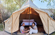 En familie sidder foran en tipi-lignende telt med seng indeni på TAIGA Delta de l'Ebre, Spanien.