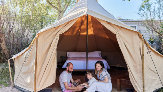Gezin zit voor een tipi-tent met bed erin bij TAIGA Delta de l'Ebre, Spanje.
