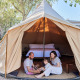 Familia sentada a la entrada de una tienda tipi con cama en TAIGA Delta de l'Ebre, España.