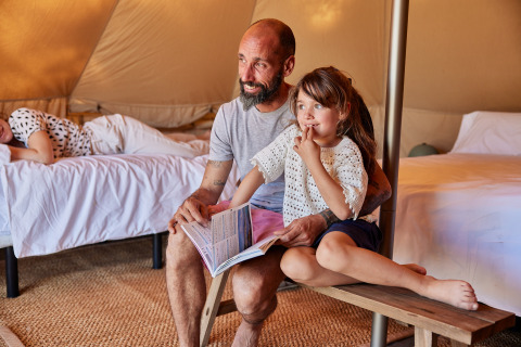 Vater und Tochter sitzen in einem Glamping-Bell-Zelt in Spanien, lesen ein Buch und genießen die Zeit.