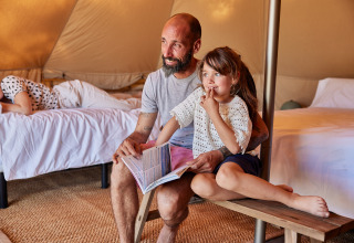 Vater und Tochter sitzen in einem Glamping-Bell-Zelt in Spanien, lesen ein Buch und genießen die Zeit.