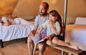Padre e hija sentados en un banco leyendo un libro dentro de una tienda Glamping Bell Tent en España.